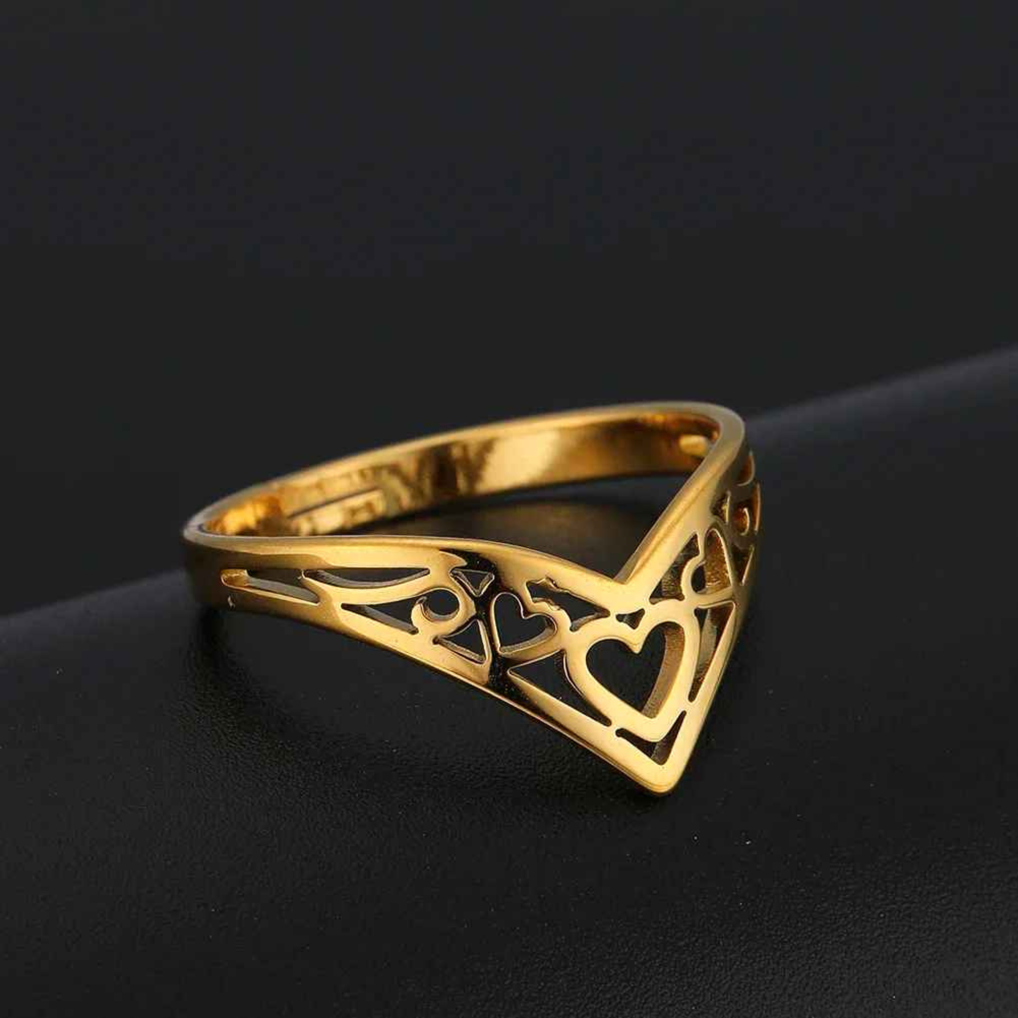 Gold ring with heart designs on a dark background
